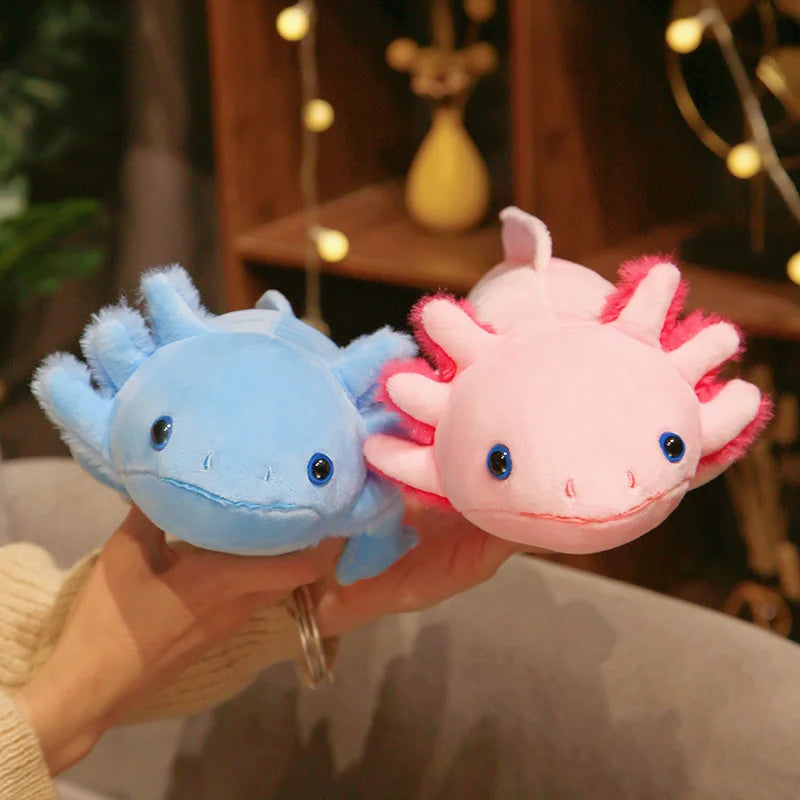 Close-up of blue and pink axolotl plush toys being held, showing their cute faces and soft plush texture.