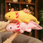 Two soft axolotl plush toys in pastel yellow and pink stacked together, featuring cute frilly gills and a cuddly long body design, held indoors for a cozy, playful look.
