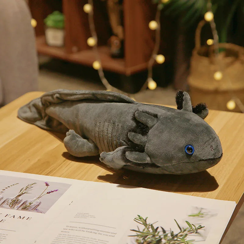 Grey axolotl plush toy resting on a wooden table with magazines, styled in a warm home interior setting.