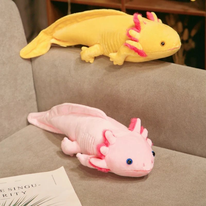 Pink and yellow axolotl plush toys displayed on a couch, featuring soft fabric and signature frilly gills.