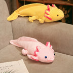 Pink and yellow axolotl plush toys displayed on a couch, featuring soft fabric and signature frilly gills.
